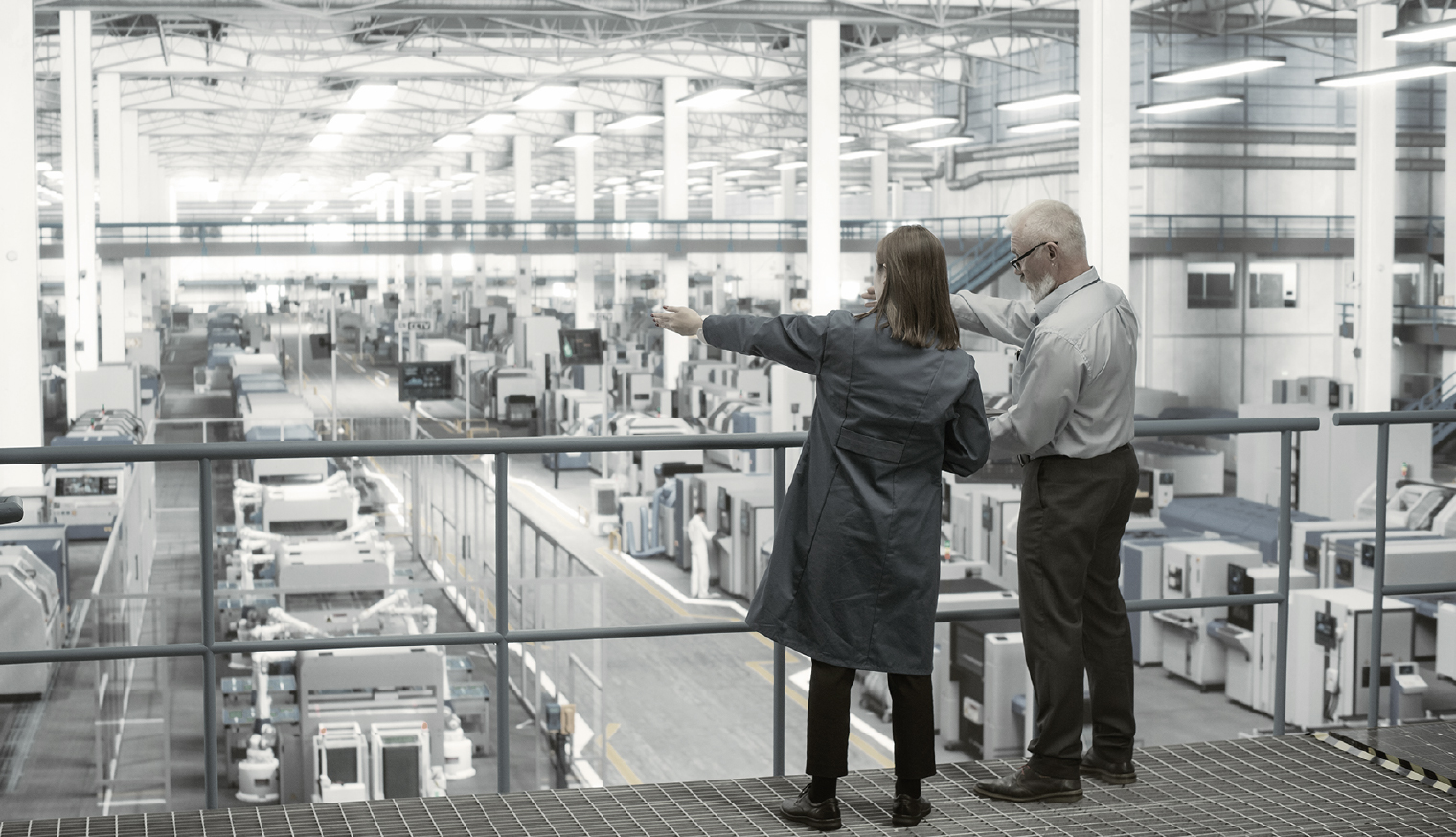 Experienced male and female engineers discuss production at a modern AI-automated electronics manufacturing plant while using laptops.