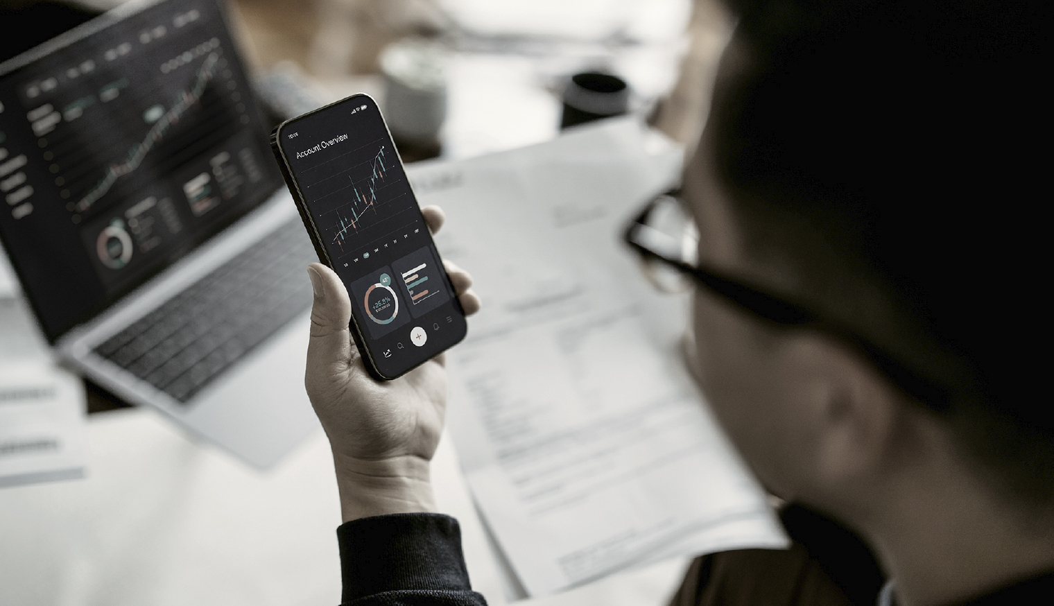 オンラインで金融と投資を管理し、スマートフォンとラップトップで株式市場の取引を分析する男性